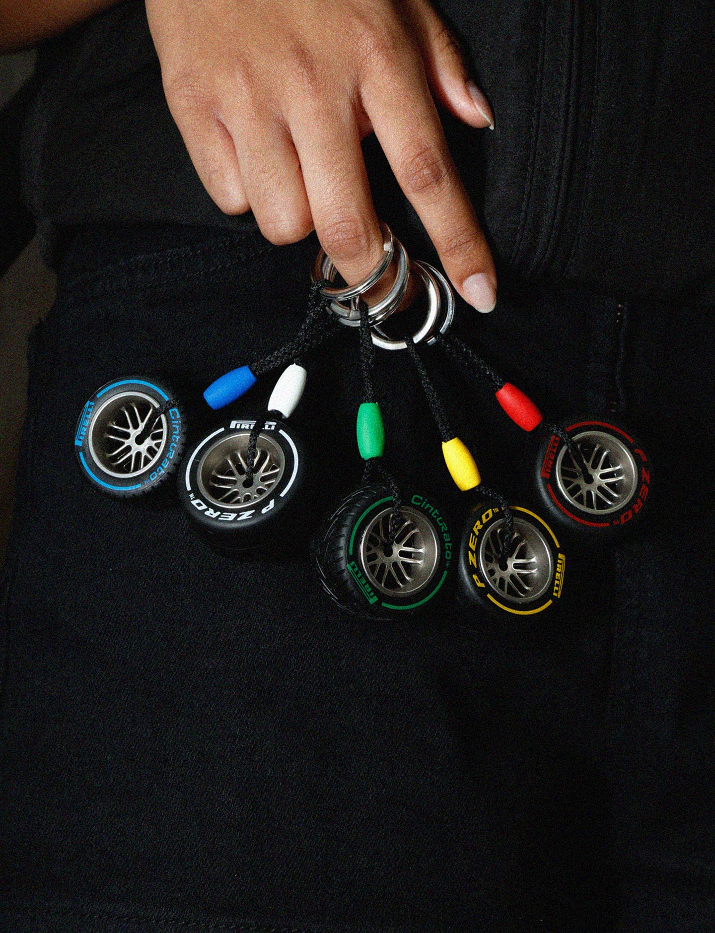 Colorful keychains with tire designs held by a hand against a black background