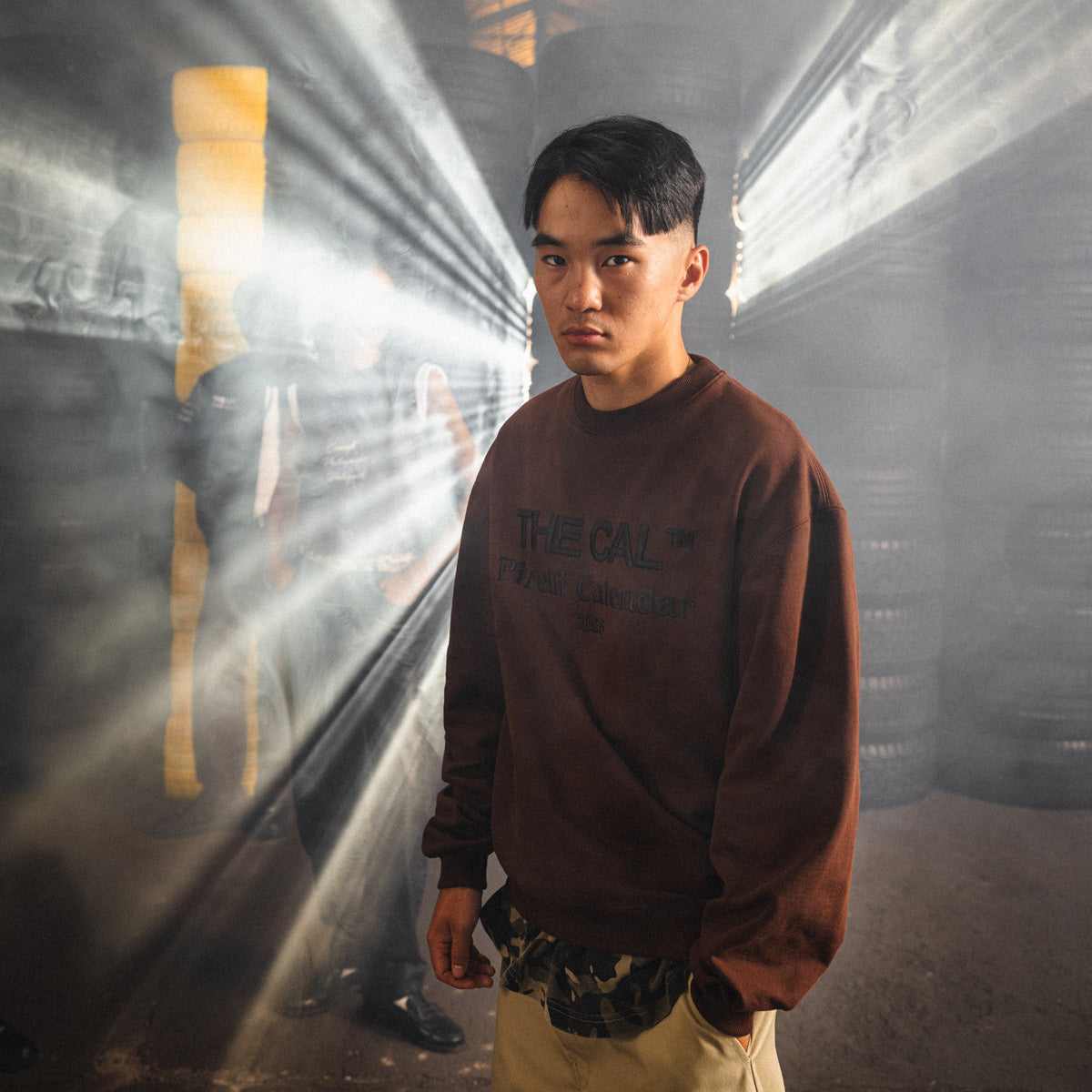 Person wearing a brown sweatshirt with text, standing in a dimly lit tunnel.