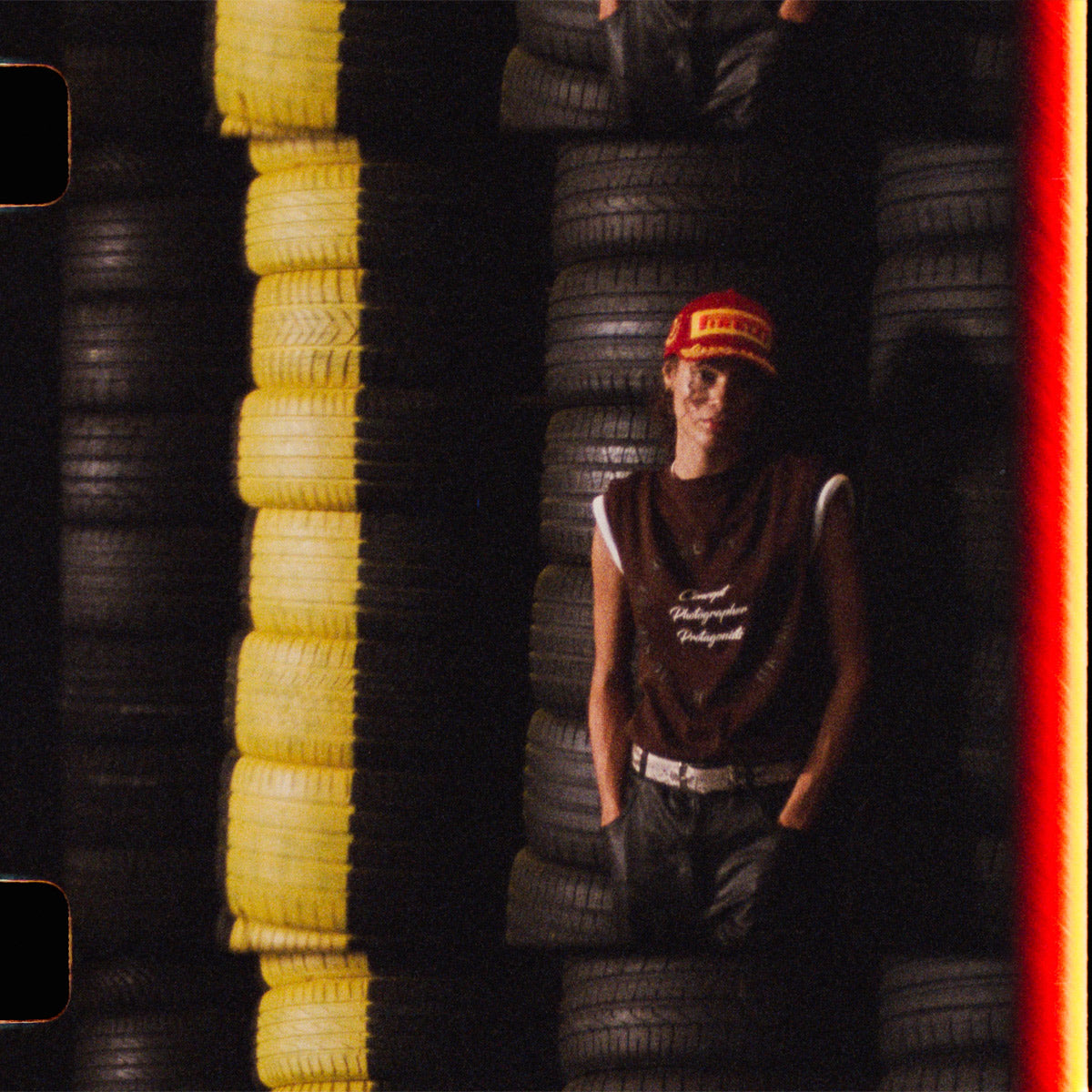 Person standing among stacked tires with a red and yellow cap
