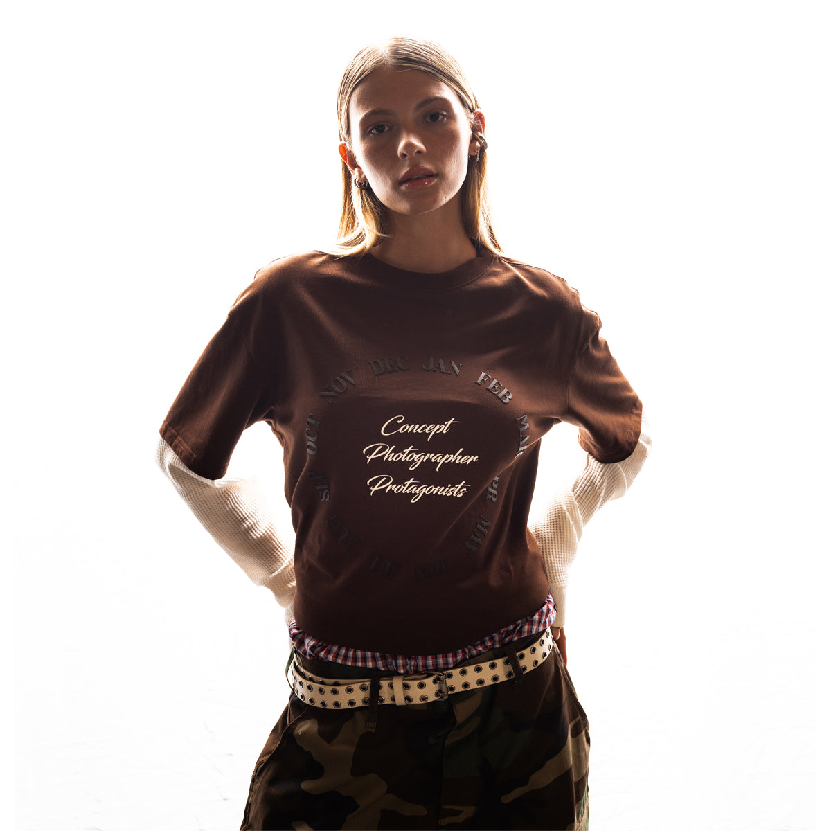 Person wearing a brown Pirelli The Cal shirt with text, standing against a white background