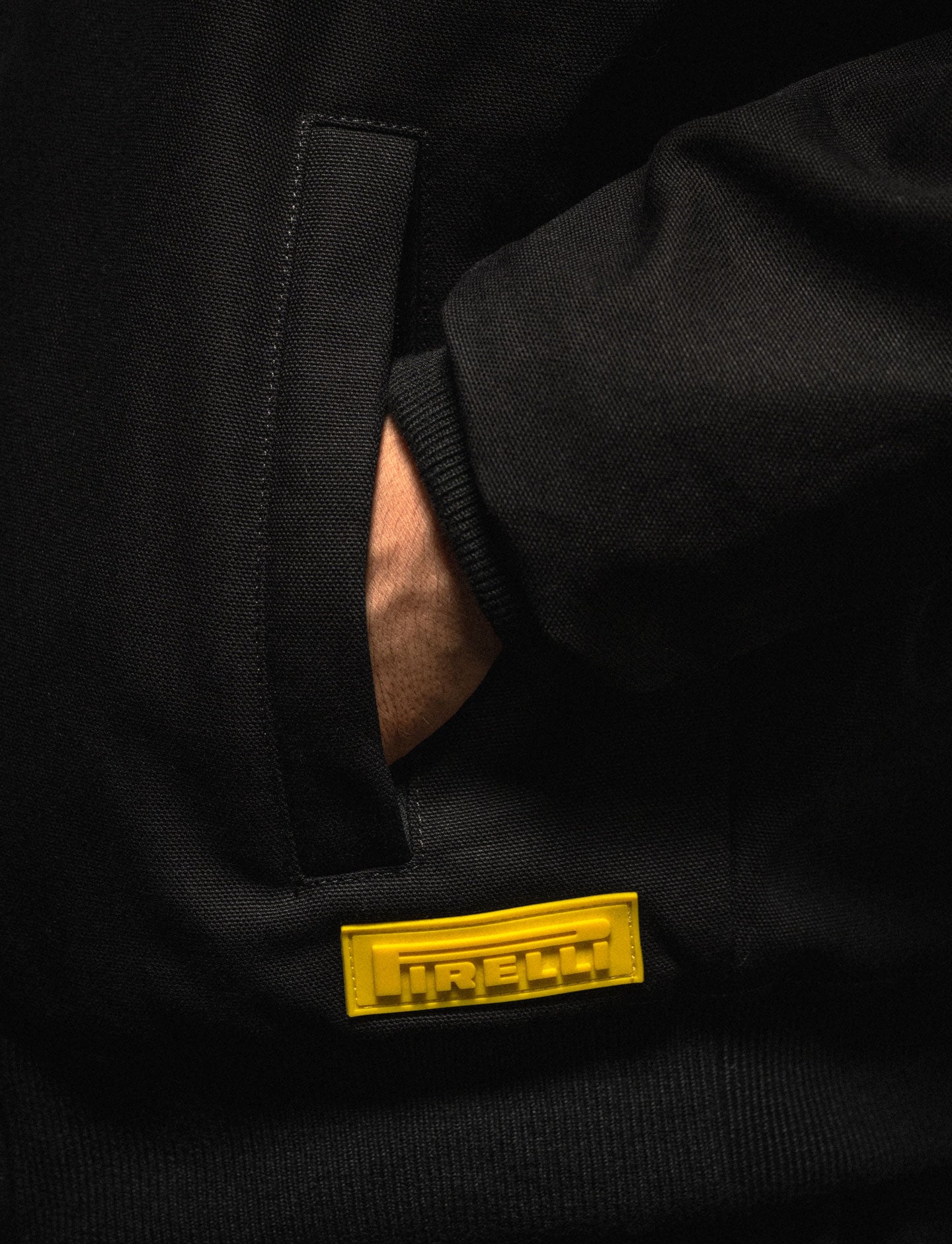 Close-up of a black jacket with a yellow rubber Pirelli logo on a dark background