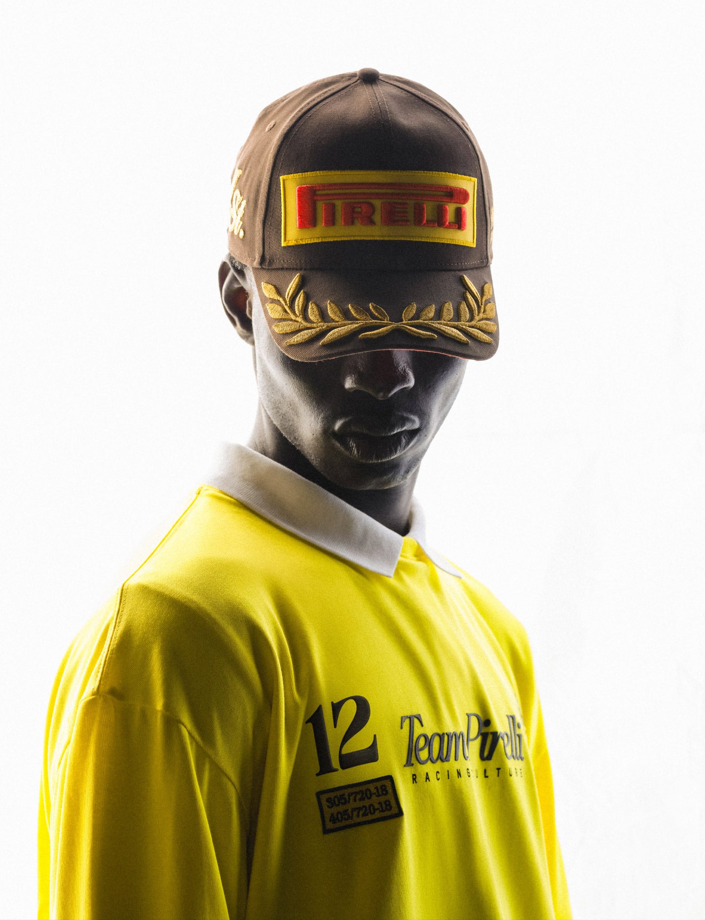 Person wearing a yellow racing long sleeve tee and cap with Pirelli logo on a white background