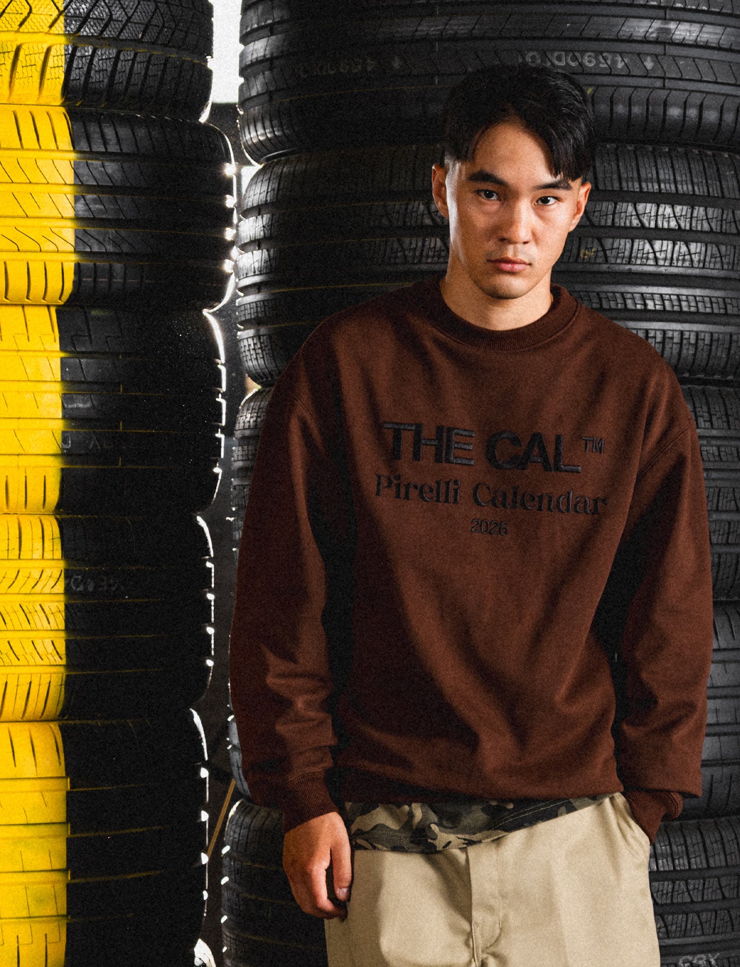 Person wearing a brown Pirelli sweatshirt with text standing in front of stacked tires.