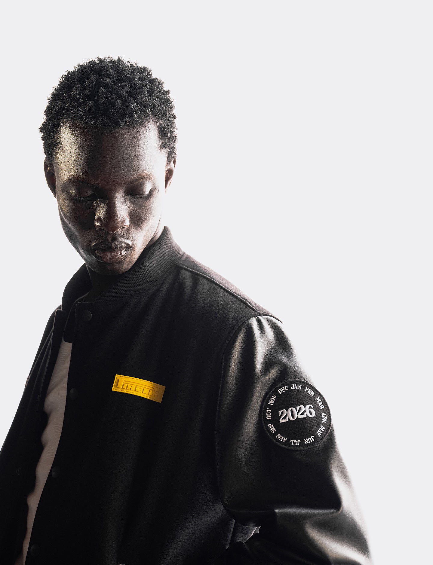 Person wearing a black jacket with a yellow Pirelli patch and '2026' patch on a white background