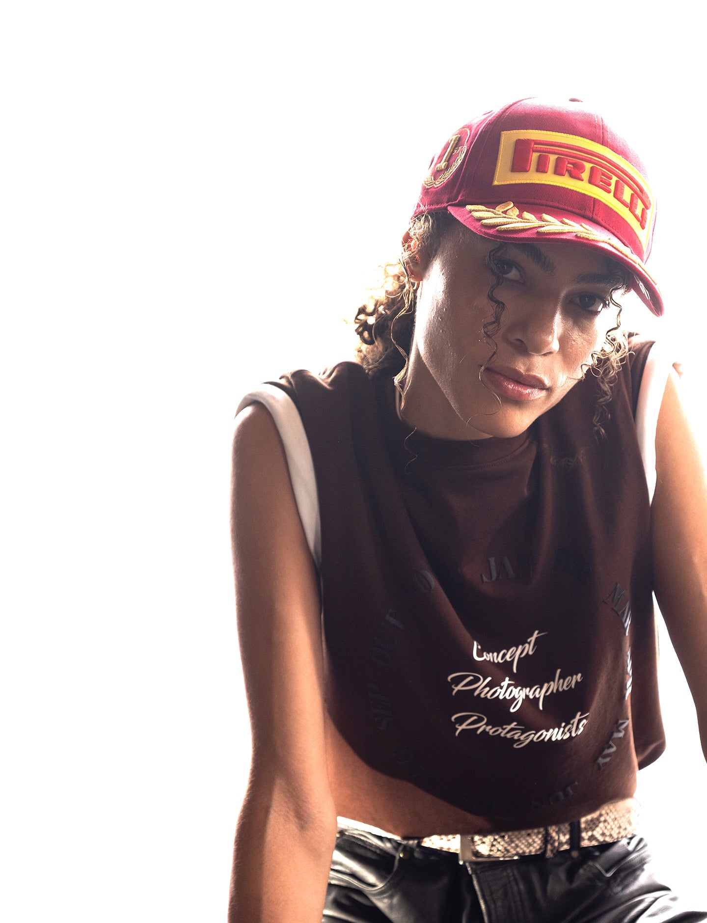 Person wearing a Pirelli cap and a sleeveless shirt with text, sitting against a white background