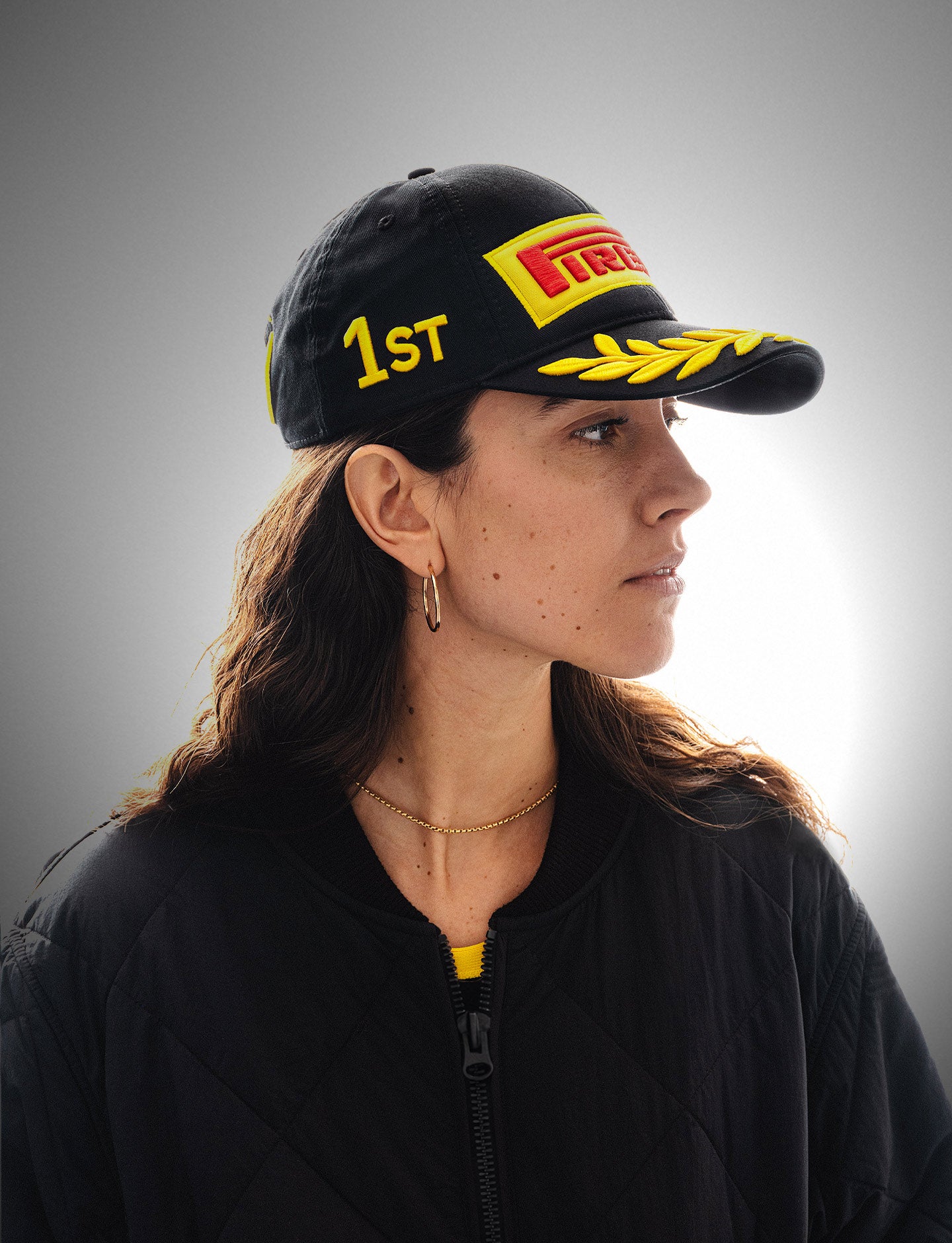 Woman wearing a black Formula 1® Pirelli Podium Cap looking to the right on a gray background