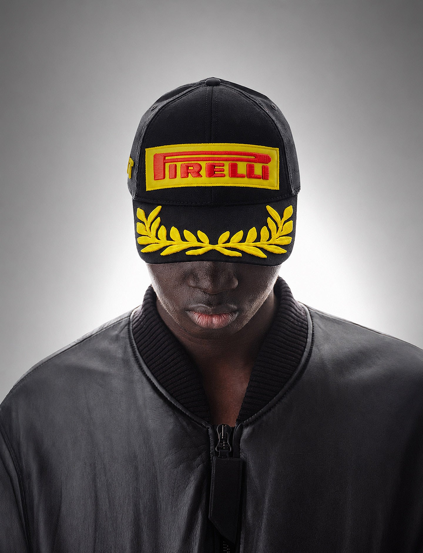 Person wearing a black cap with Pirelli logo and yellow design on a gray background