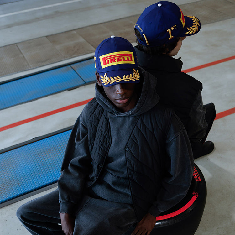 two men in blue Pirelli Podium Caps sitting on Pirelli tyre