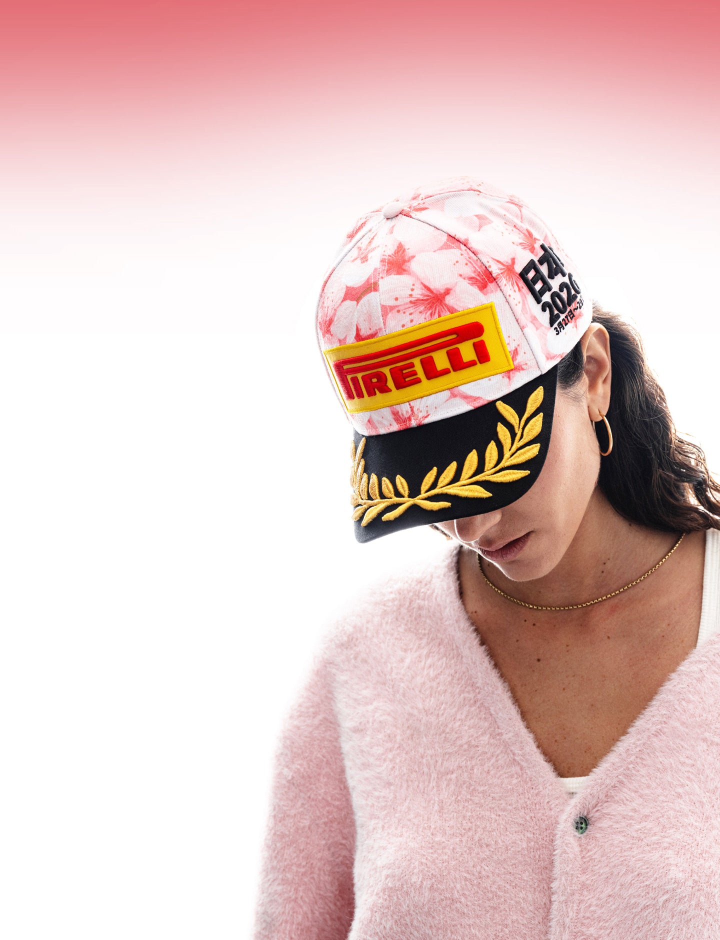 Person wearing a Pirelli branded racing cap with cherry blossom design on a pink background