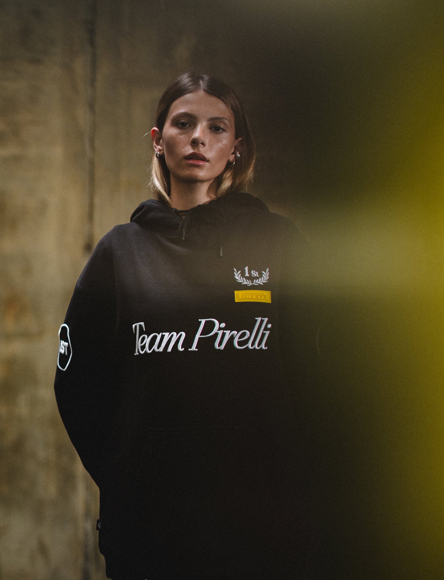 Person wearing a black hoodie with 'Team Pirelli' text against a textured wall.