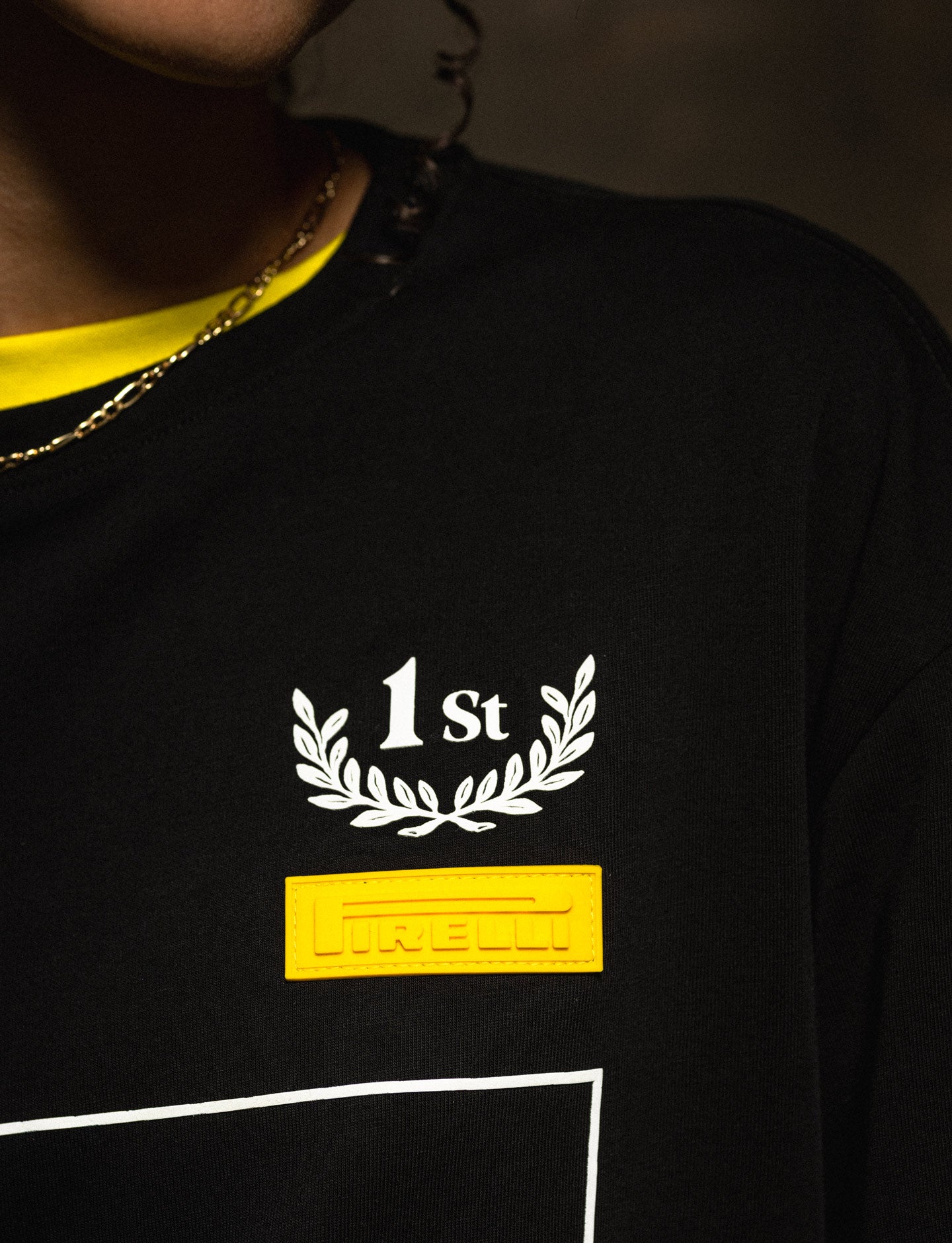 Black Pirelli shirt with '1st' and laurel wreath design, worn by a person.