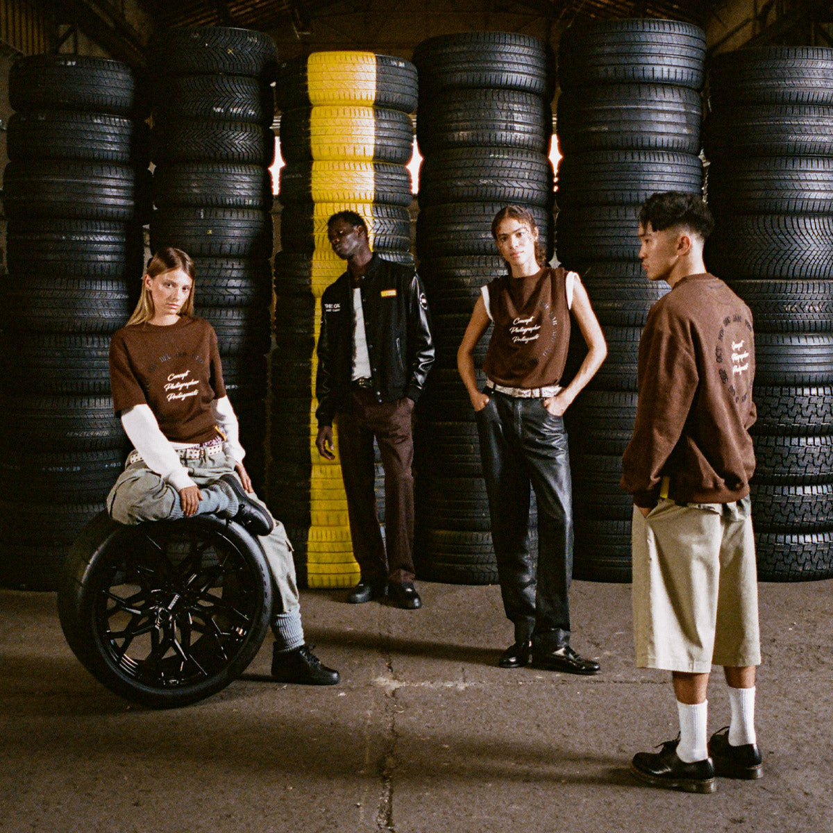 Four people standing in a warehouse with stacks of tires in the background