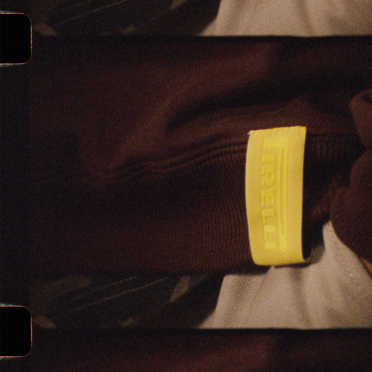 Close-up of a brown crewneck with a yellow 'Pirelli' logo.