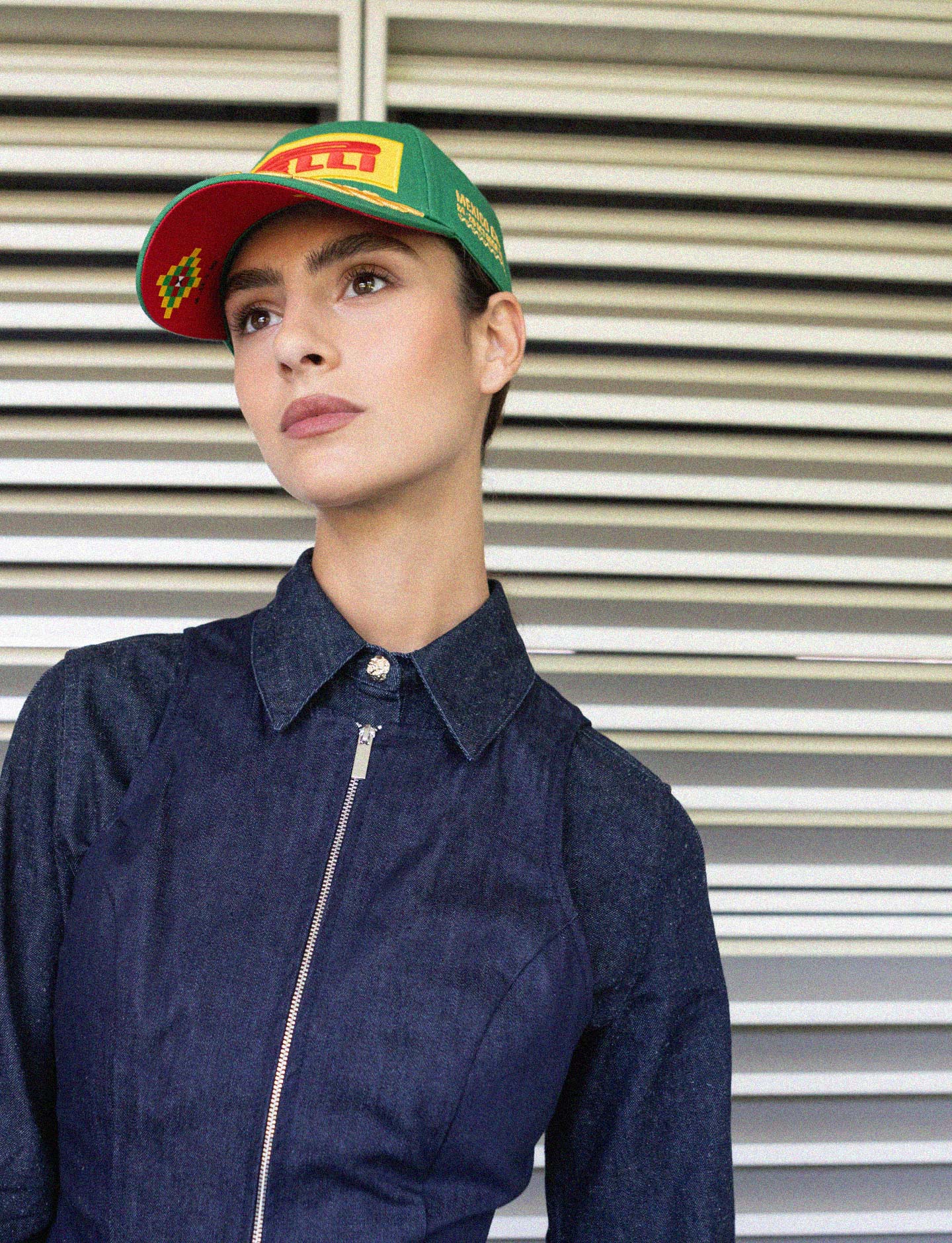 Person wearing a denim jacket and a cap with a Pirelli logo against a metallic shutter background