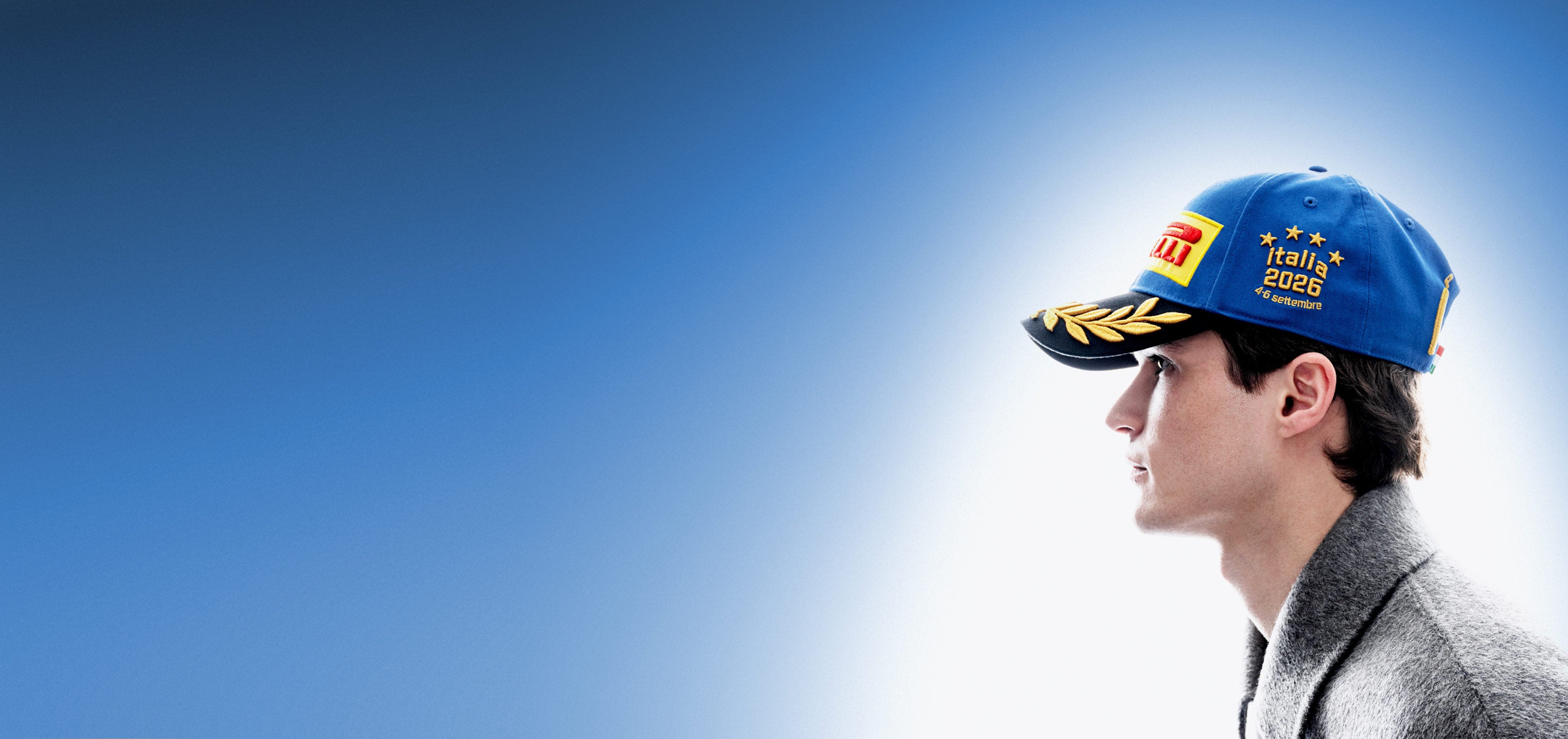 A man in profile wearing a blue Pirelli Podium Cap 2026 Monza against a blue-to-white gradient background.
