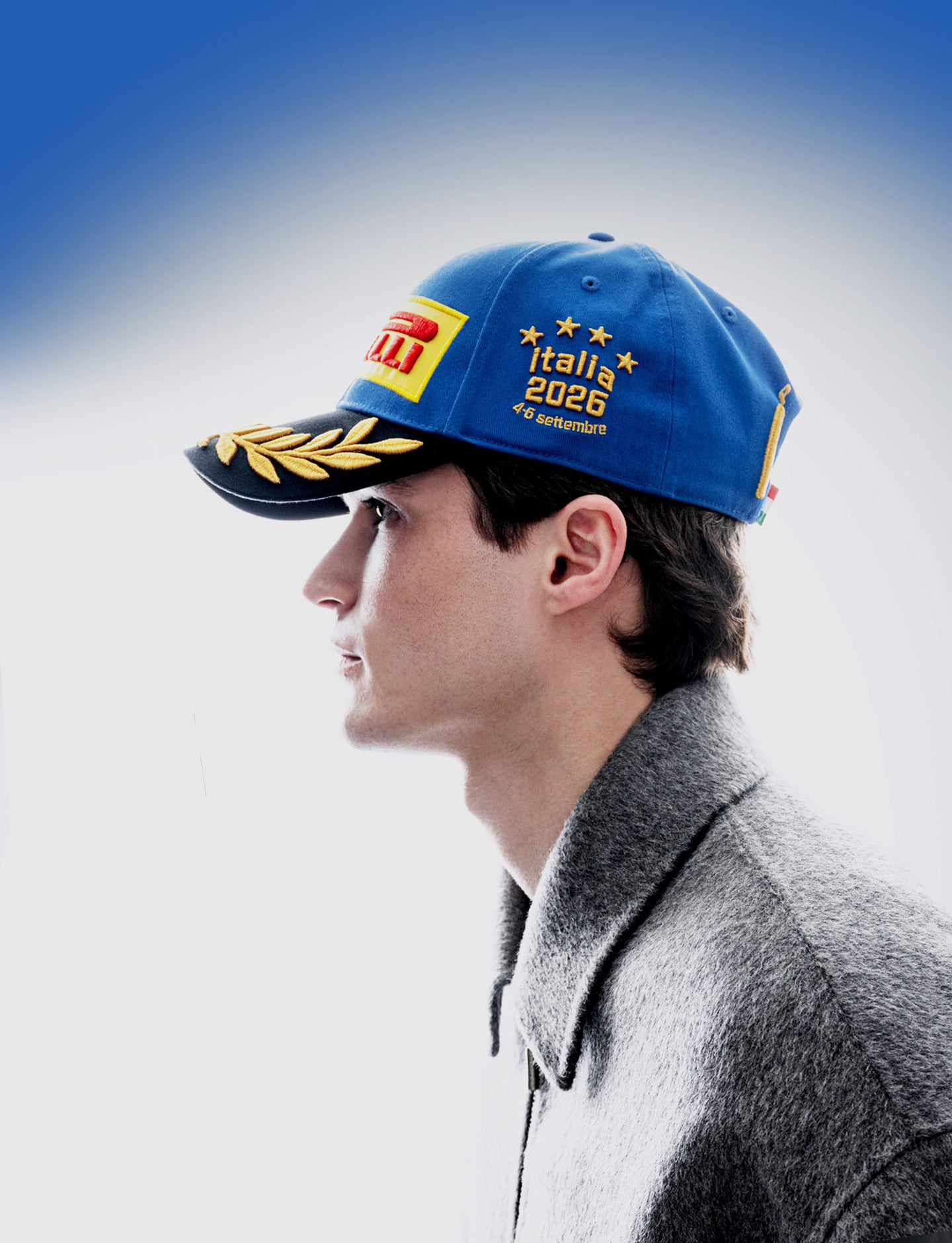 A man in profile wearing a blue Pirelli Podium Cap 2026 Monza against a blue-to-white gradient background.
