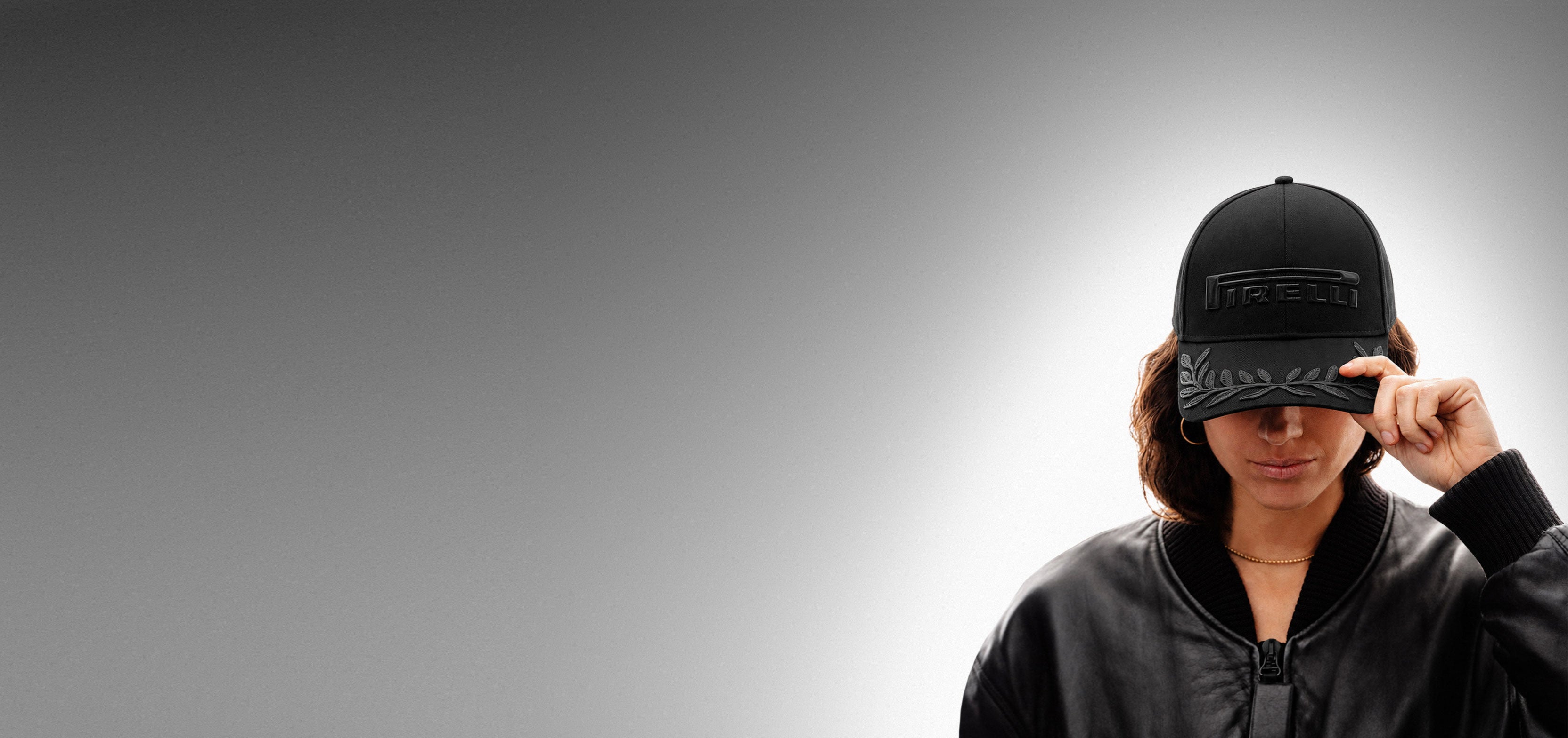 Woman wearing a black on black Pirelli cap on a gray gradient background