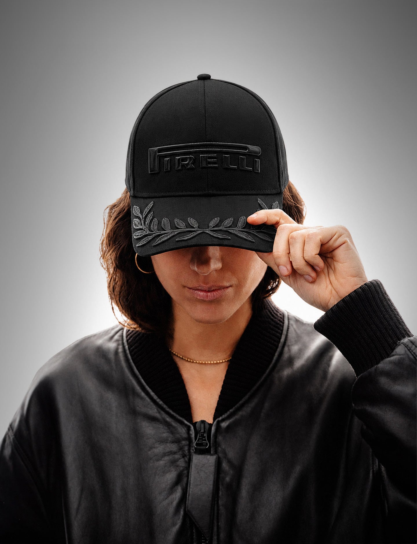 Woman wearing a black on black Pirelli cap on a gray gradient background