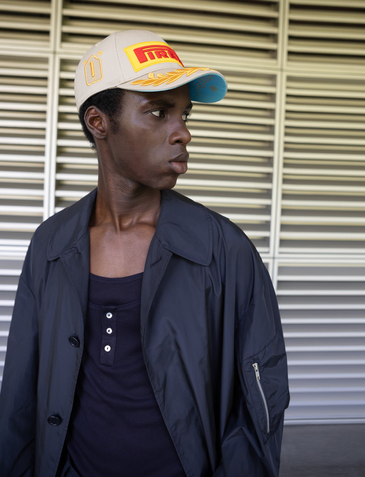 Person wearing a beige Pirelli cap with a logo against a metallic background