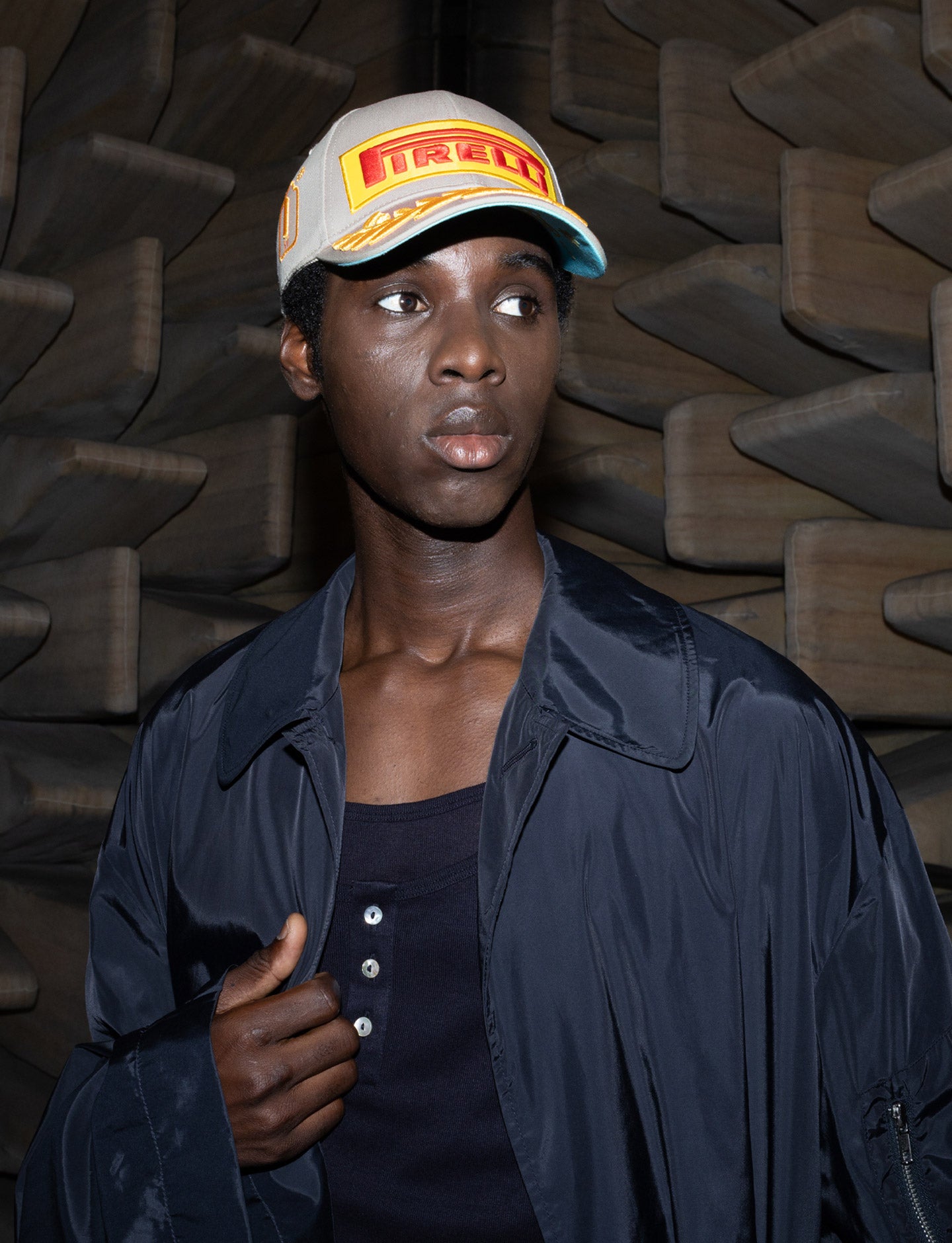 Person wearing a cap with a Pirelli logo against a textured dark background