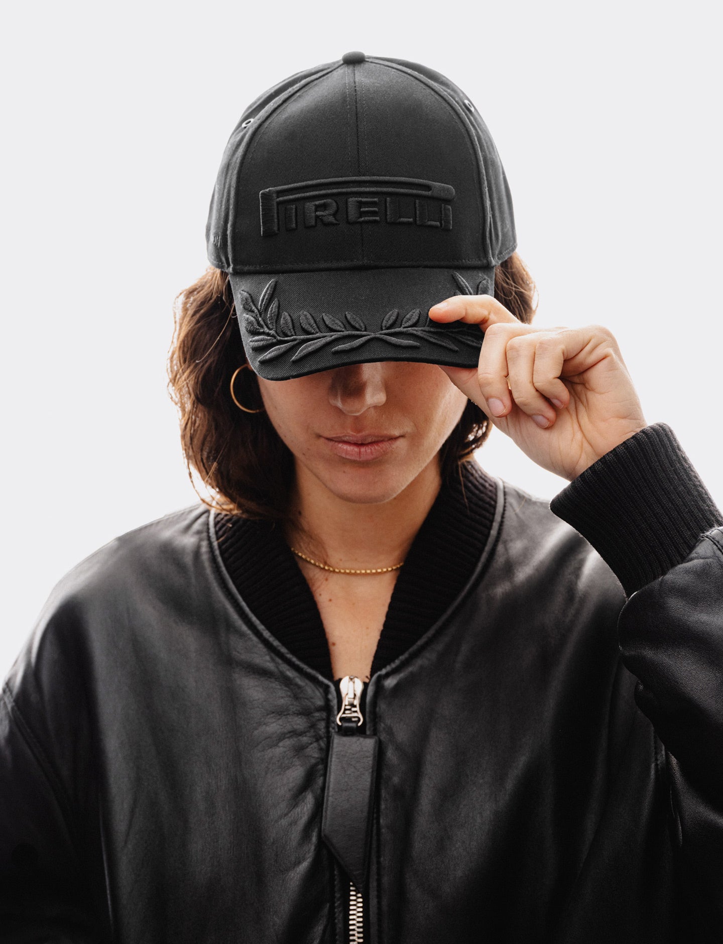 Person wearing a black cap with a black Pirelli logo on a light gray background