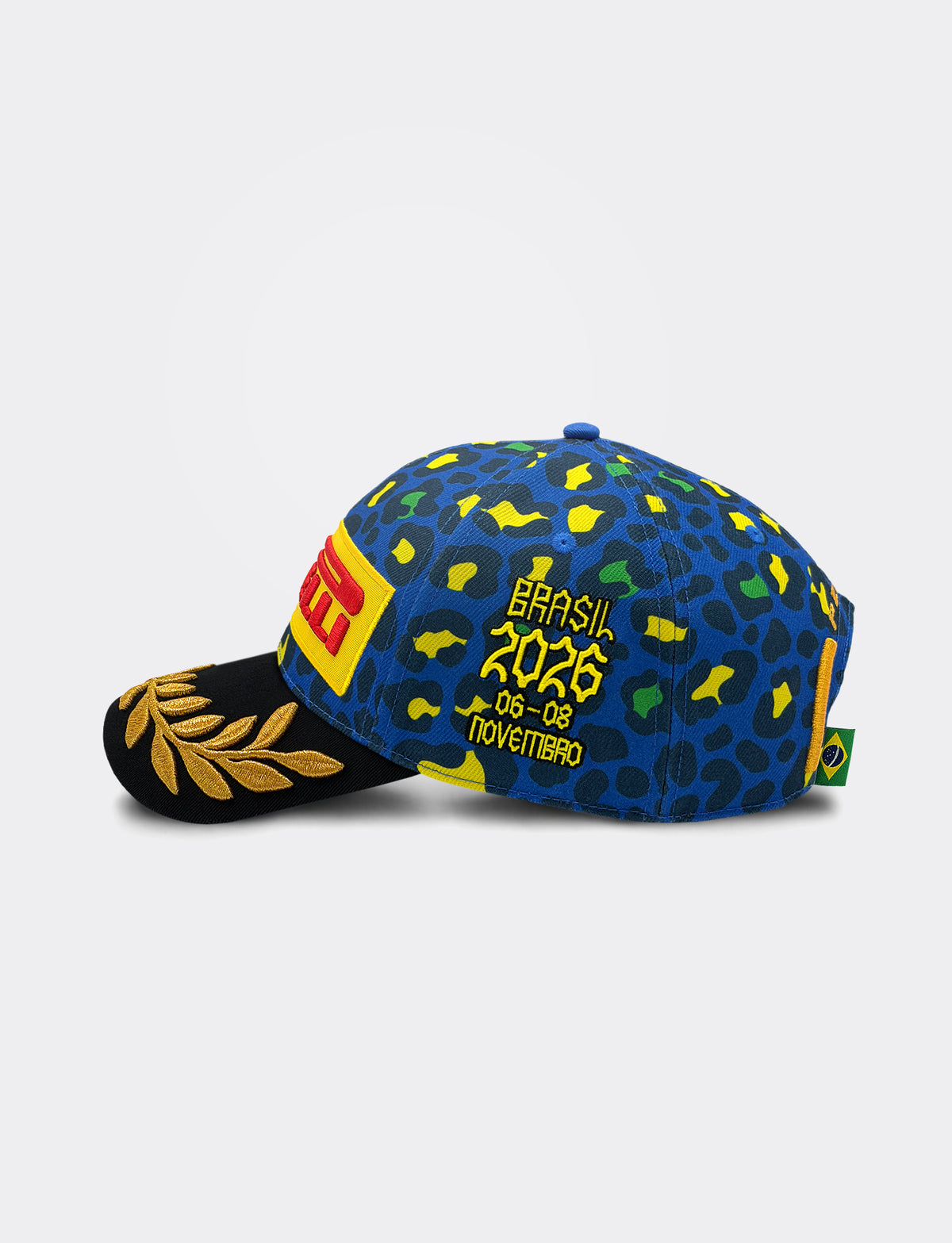 A blue Pirelli baseball cap with a jaguar print pattern in yellow, green, and black, featuring yellow embroidered text that reads 'Brasil 2026' and '06-08 Novembro'. The brim is black with a gold laurel leaf design, and a red and yellow Pirelli logo patch is visible on the front side.
