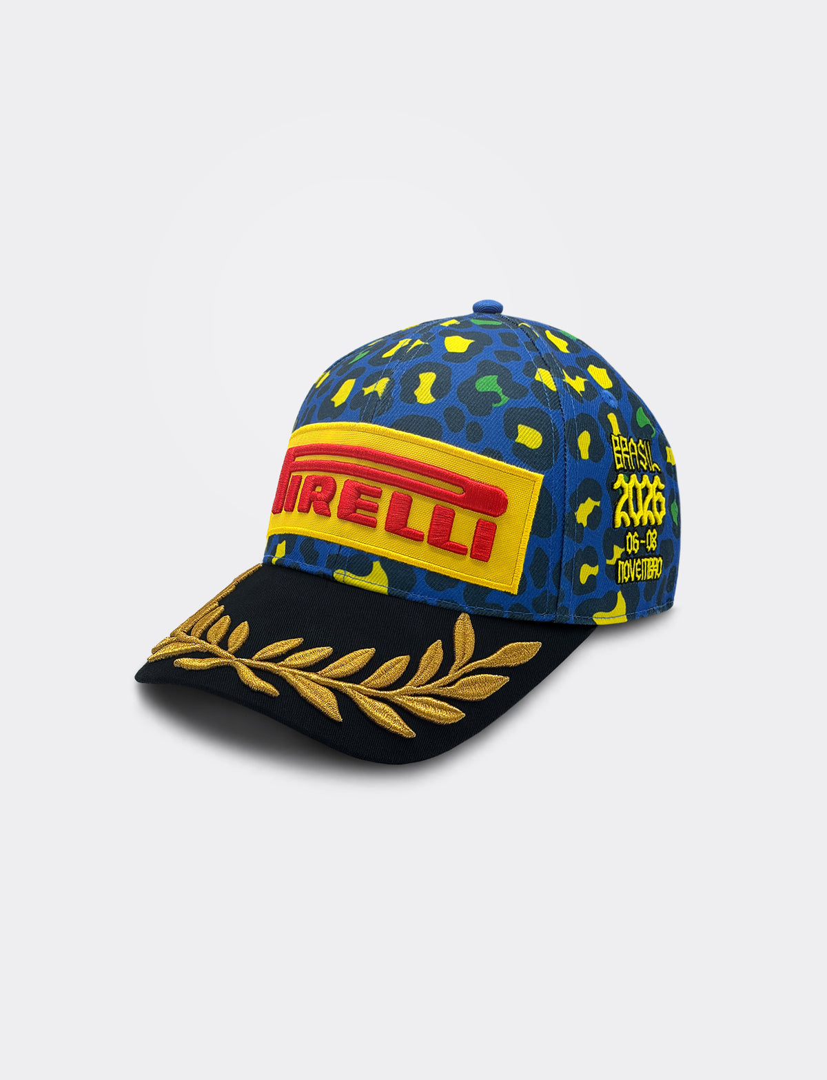 A Pirelli Podium Cap 2026 Brazil featuring a blue and yellow camouflage pattern on the crown, a large red and yellow Pirelli logo patch on the front, and a black brim decorated with a gold laurel leaf embroidery.