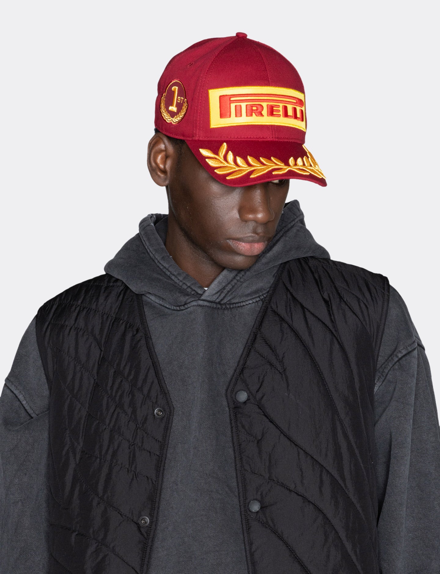 Person wearing a red cap with Pirelli logo and black jacket on gray background
