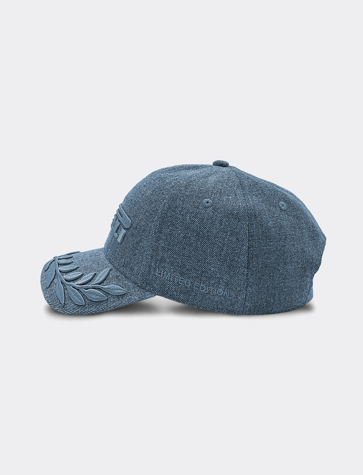 A blue denim Pirelli baseball cap shown from a side profile view against a light gray background. The cap features an embroidered laurel leaf design on the brim and subtle tonal embroidery "LIMITED EDITION" texton the side.