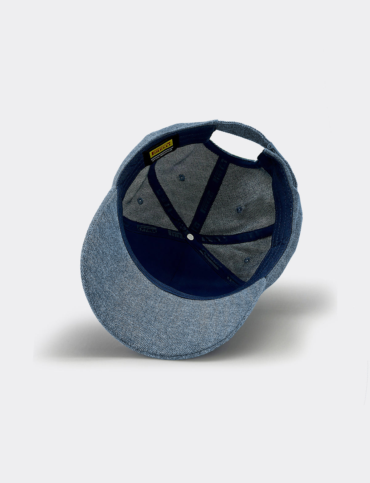 A structured Pirelli baseball cap shown from a rear three-quarter view, featuring a denim blue fabric crown and brim with a dark navy blue interior and structural straps.