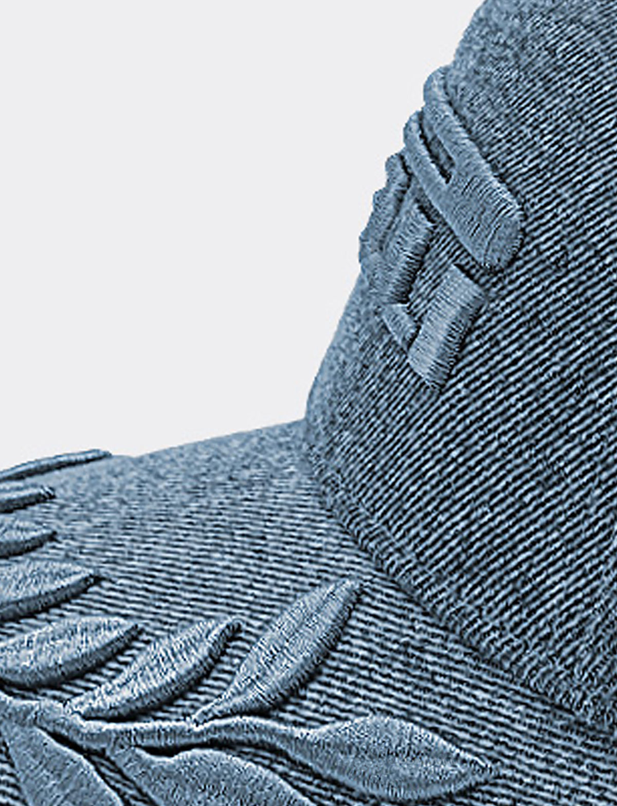 Close-up detail of a denim Pirelli capwith raised leaf embroidery and a stitched logo on the side, shown against a plain light background.