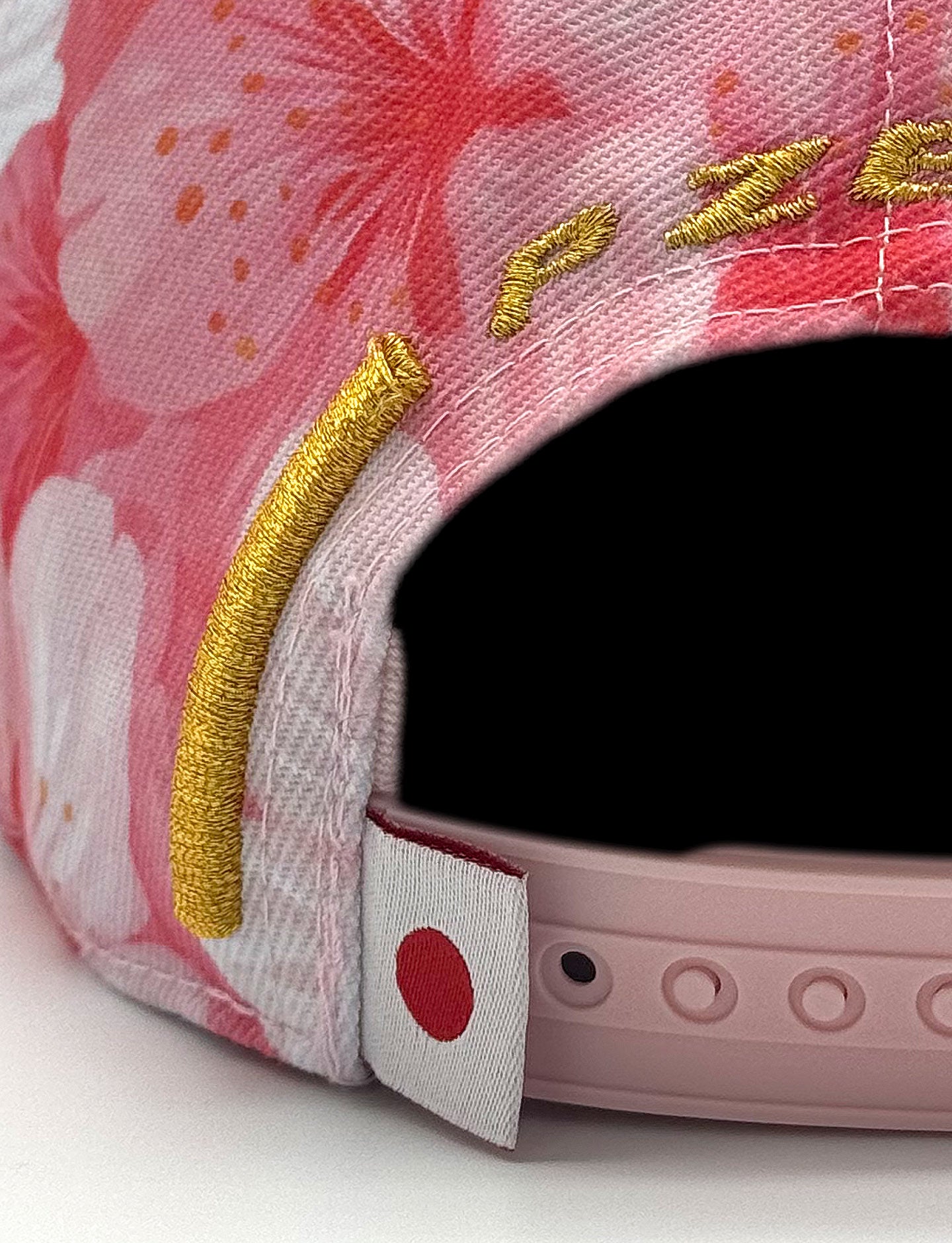 Close-up of a pink cap with floral patterns, Japanese flag label and gold accents on a white background