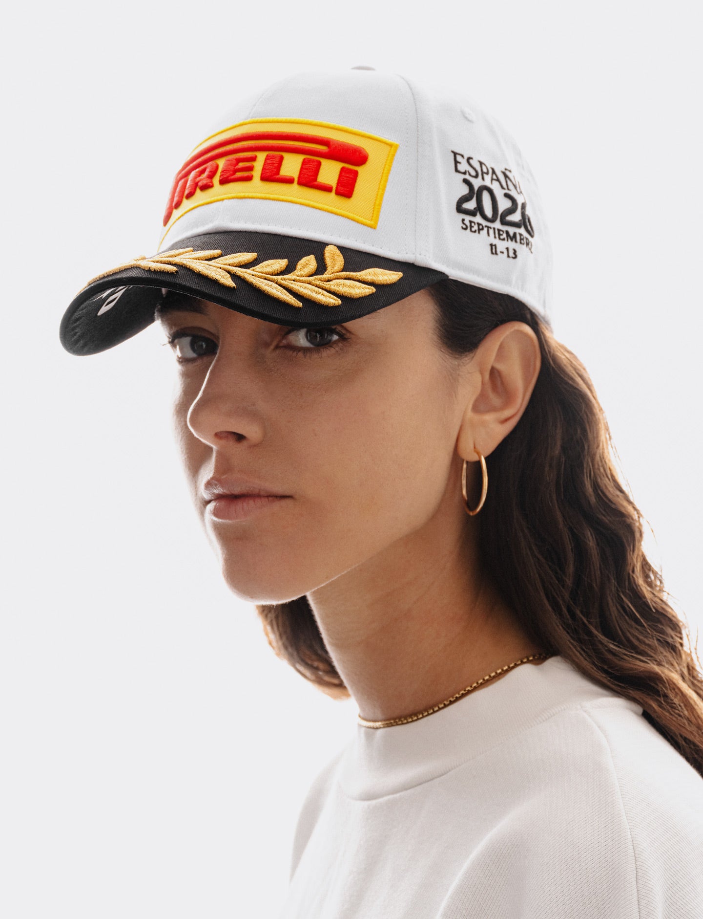 Woman wearing a Pirelli Podium Cap 2026 Madrid looking slightly to the left and also wearing a white woven sweatshirt