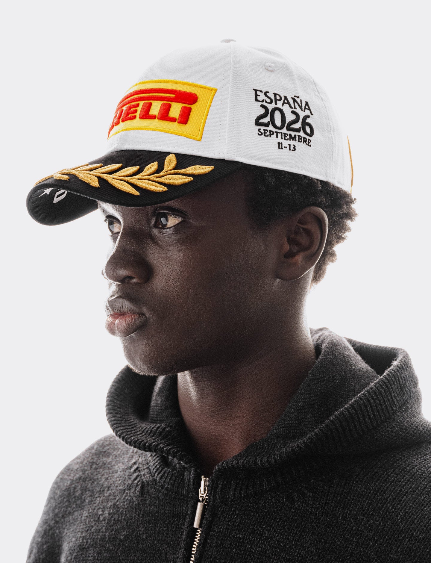 Man wearing a Pirelli Podium Cap 2026 Madrid looking to the left and also wearing a black woven hoodie
