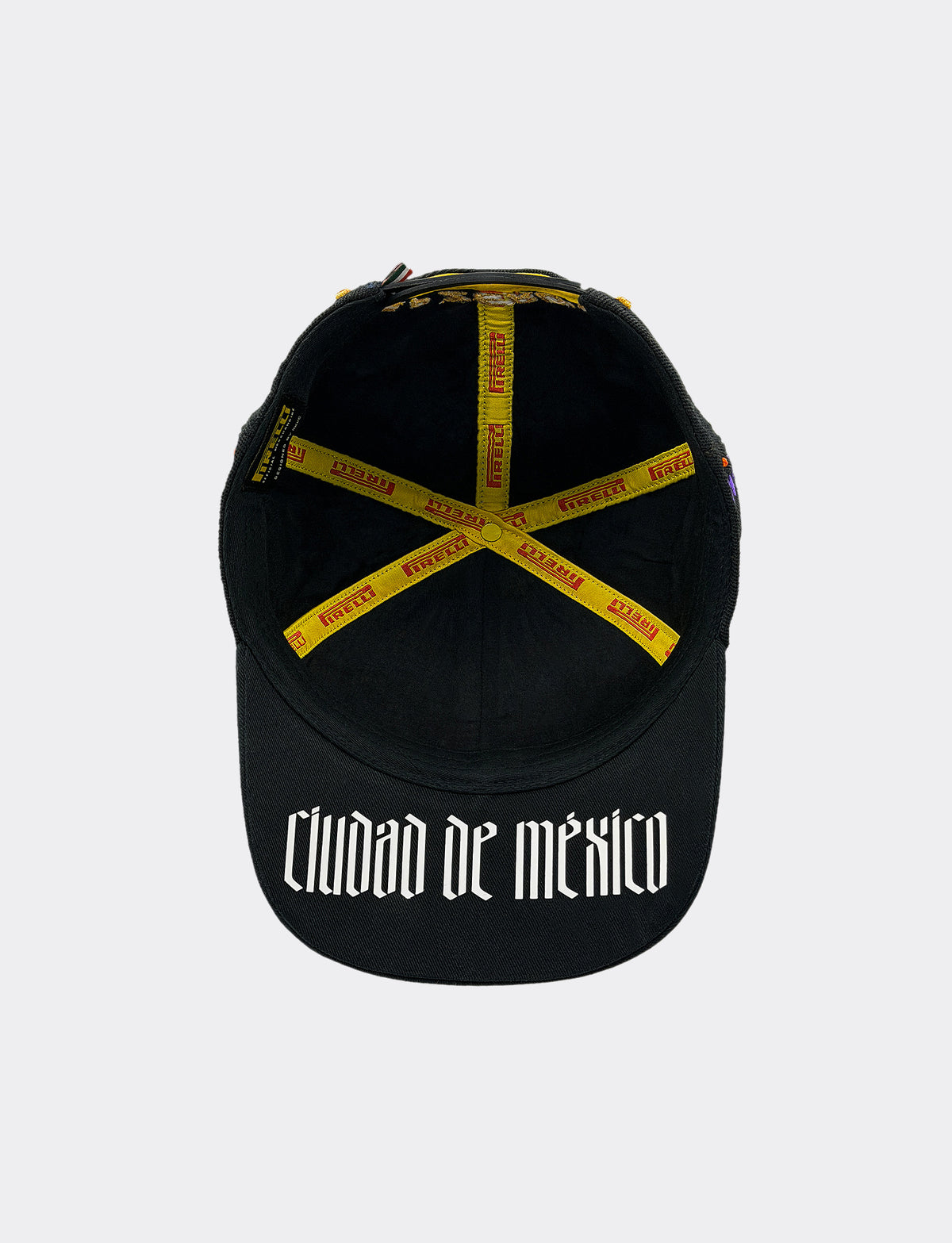 A black baseball cap underside view with 'CIUDAD DE MÉXICO' printed in white Gothic font on the front, featuring yellow & red Pirelli straps across the crown