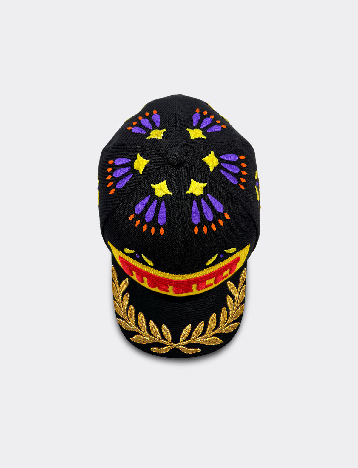 A black baseball cap featuring a colorful embroidered design with purple and yellow motifs on the crown, a red and yellow Pirelli logo on the brim, and a gold laurel wreath embroidery on the underside of the brim, shown against a light gray background.