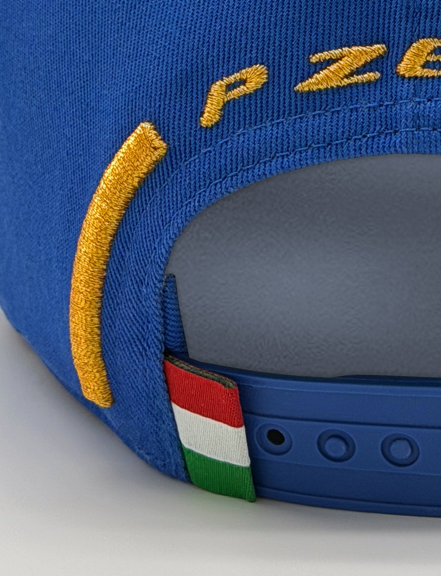 Close-up of a blue Pirelli baseball cap showing the back strap, yellow embroidered lettering, and a small Italian flag tab.