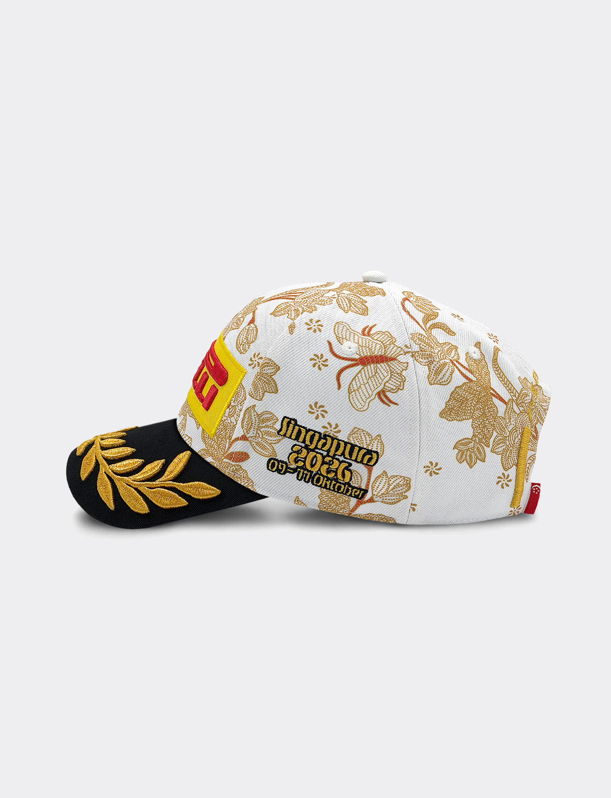 Left side view of Pirelli Podium Cap 2026 Singapore featuring a white crown with orange/brown floral patterns, a black brim with gold leaf embroidery, and yellow and red graphic Pirelli logo on the front.