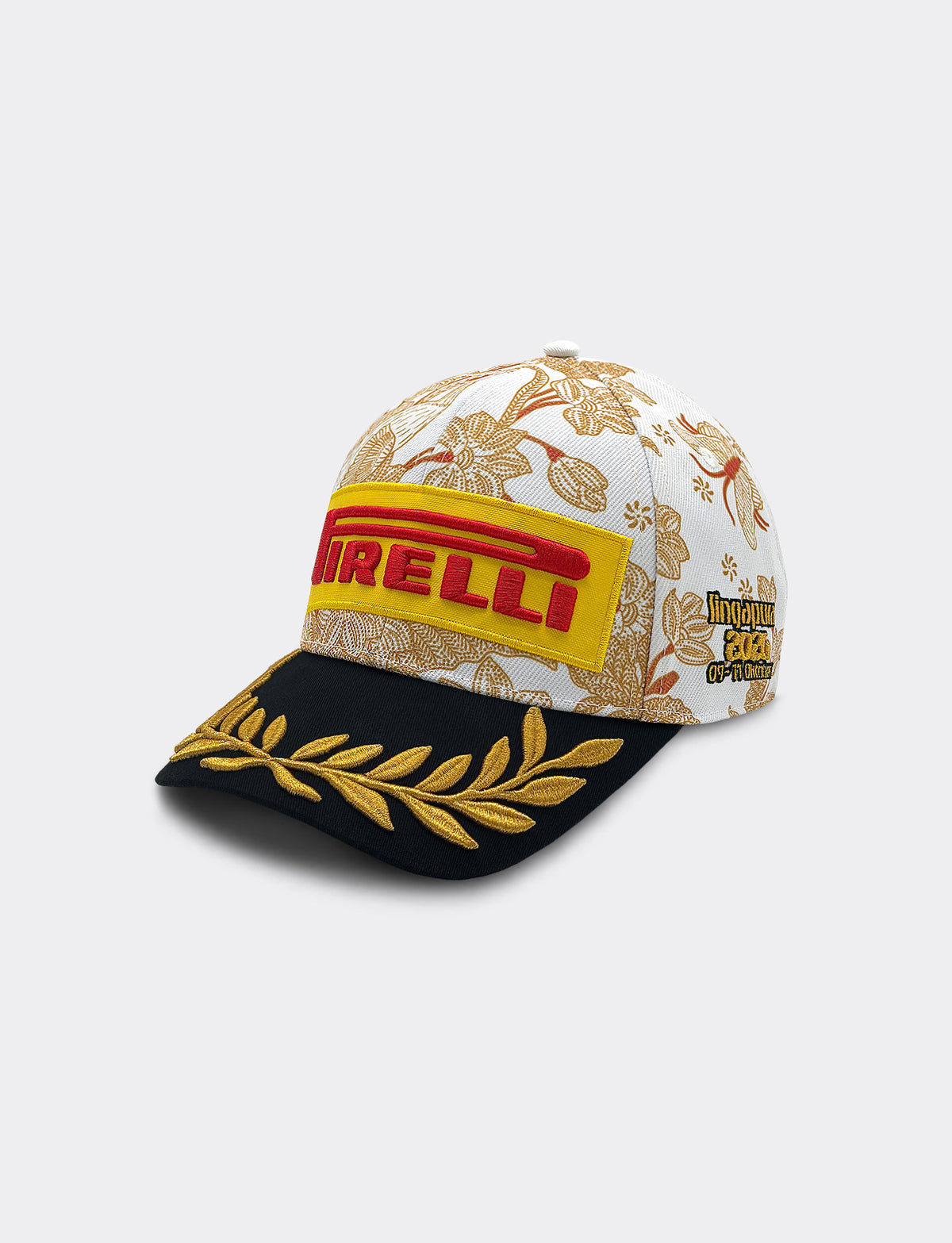 Left 45 degree view of Pirelli Podium Cap 2026 Singapore featuring a white crown with orange/brown floral patterns, a black brim with gold leaf embroidery, and yellow and red graphic Pirelli logo on the front.