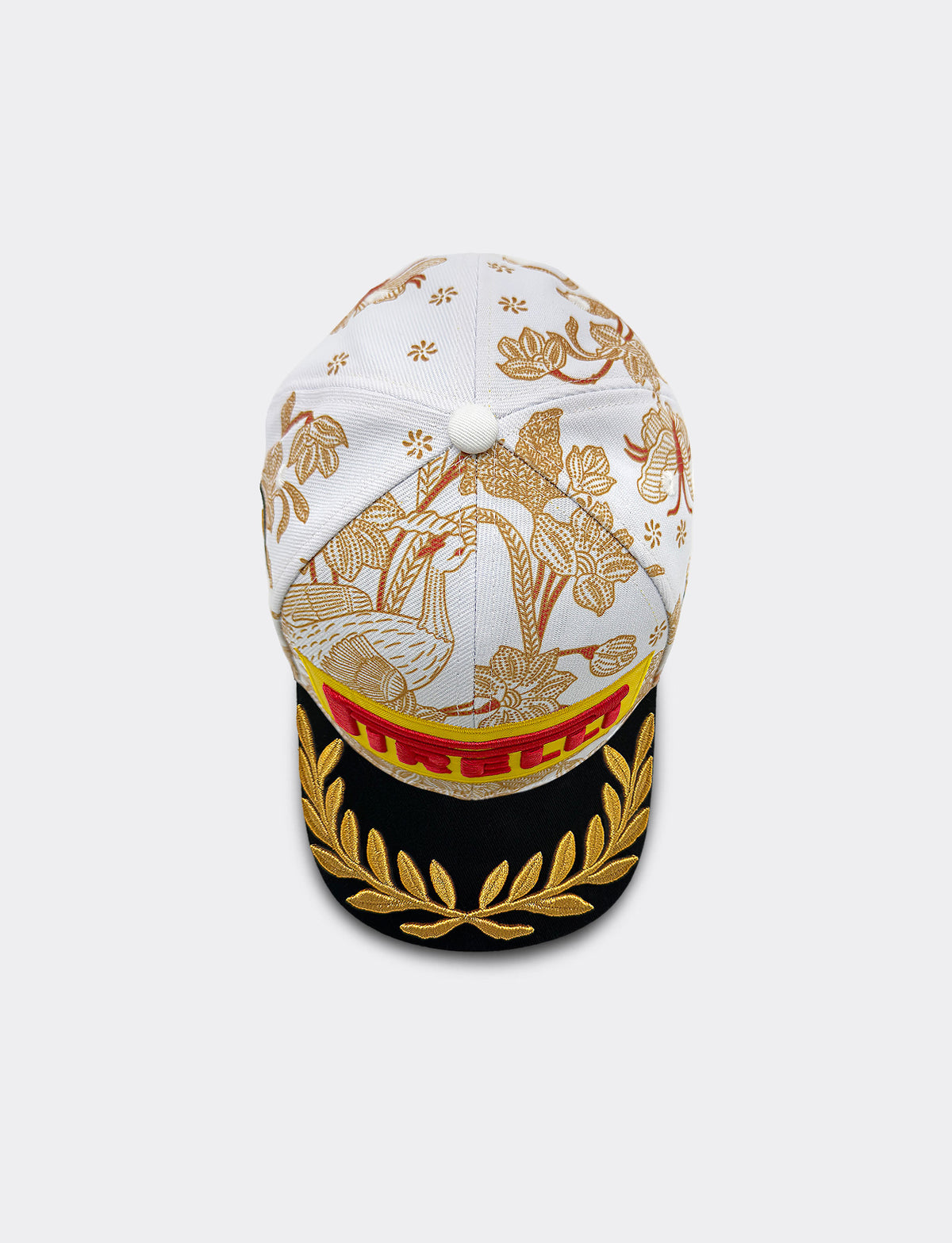 Top view of Pirelli Podium Cap 2026 Singapore featuring a white crown with orange/brown floral patterns, a black brim with gold leaf embroidery, and yellow and red graphic Pirelli logo on the front.