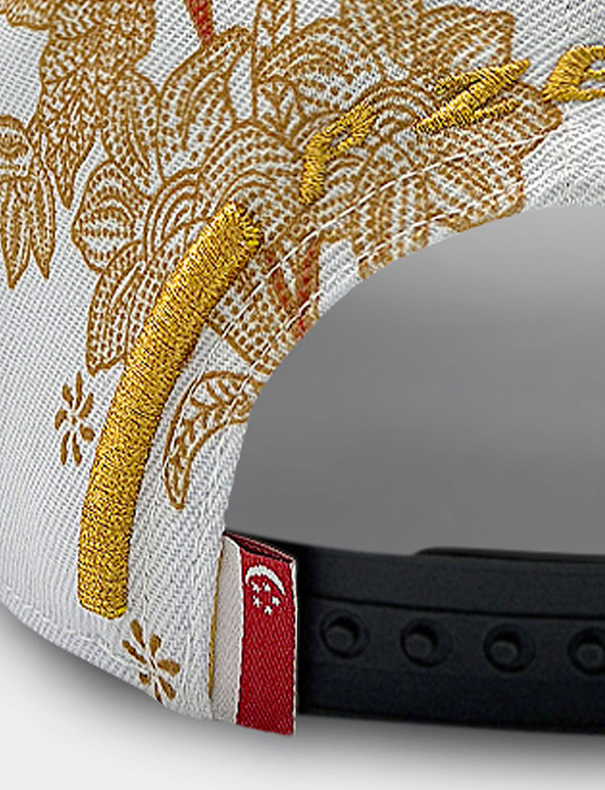 Closeup of Pirelli Podium Cap 2026 Singapore showing gold embroidered "P ZERO" on a white cap with orange/brown floral print and a Singapore flag on the snapback closure.