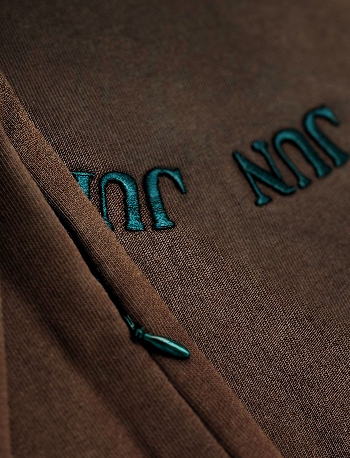 Brown fabric with teal embroidered text on a close-up shot of zipper under arms