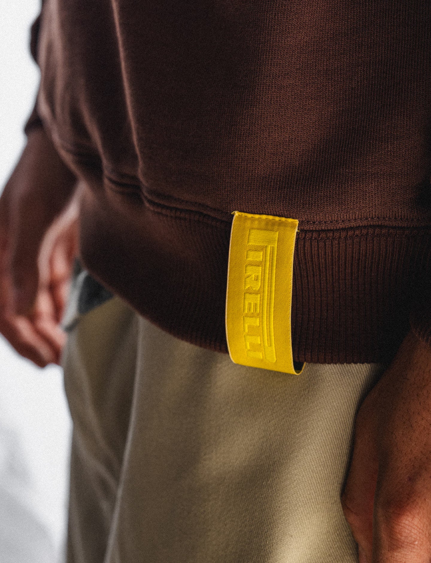 Close-up of a brown Pirelli sweatshirt with a yellow Pirelli logo on the sleeve.