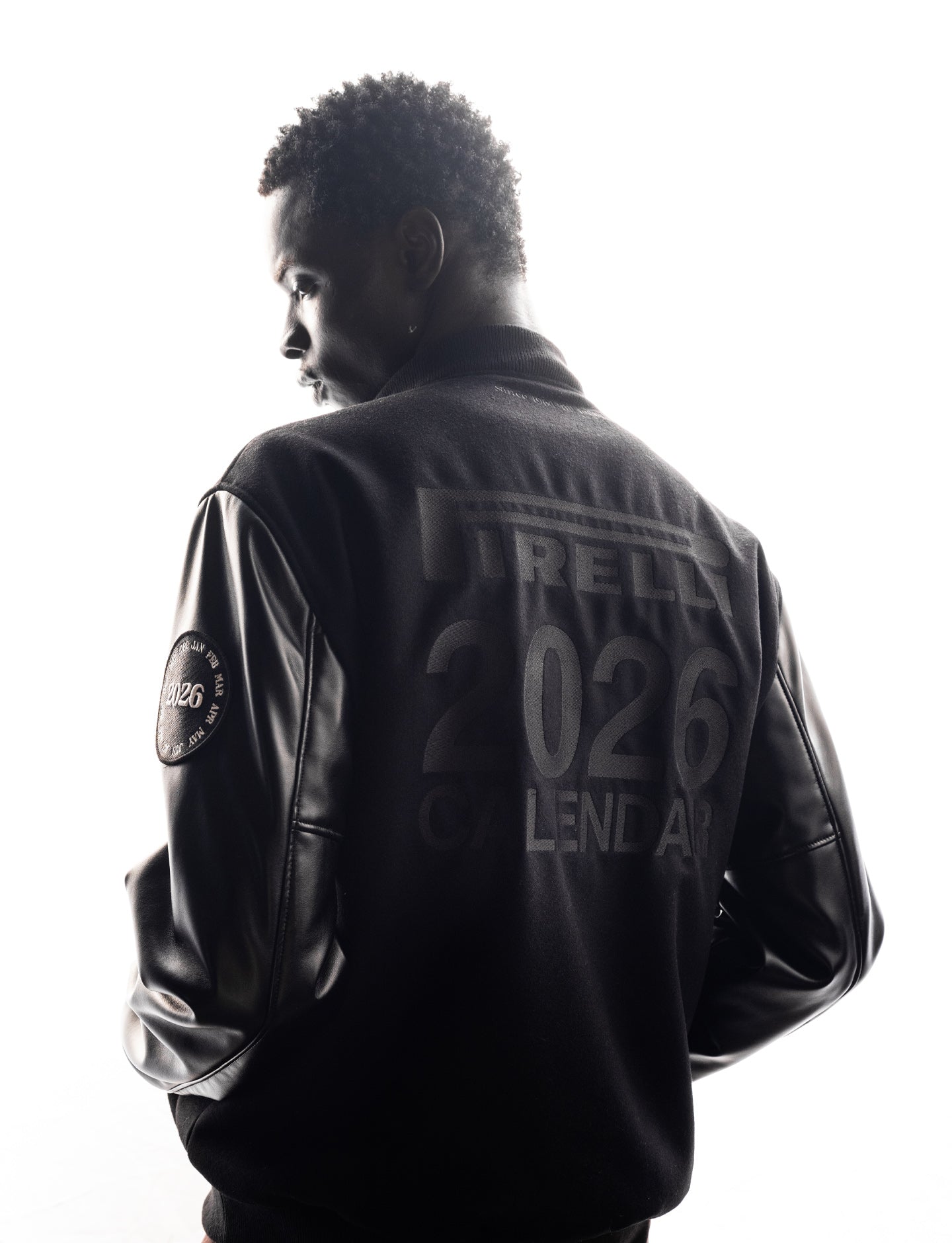 Person wearing a black Pirelli canvas and leather jacket with text and logos on the back, on a white background