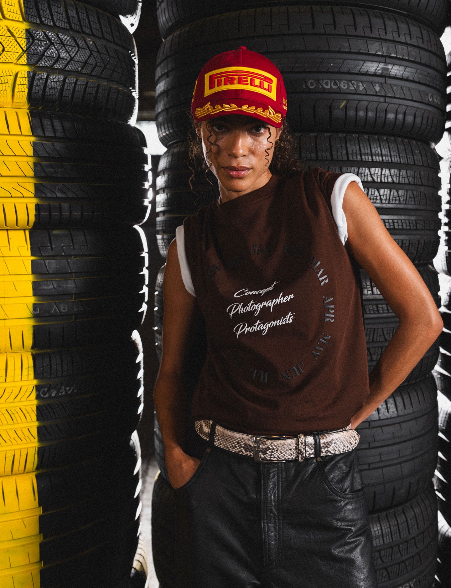 Person wearing a Pirelli cap and brown tee shirt standing among stacked tires.