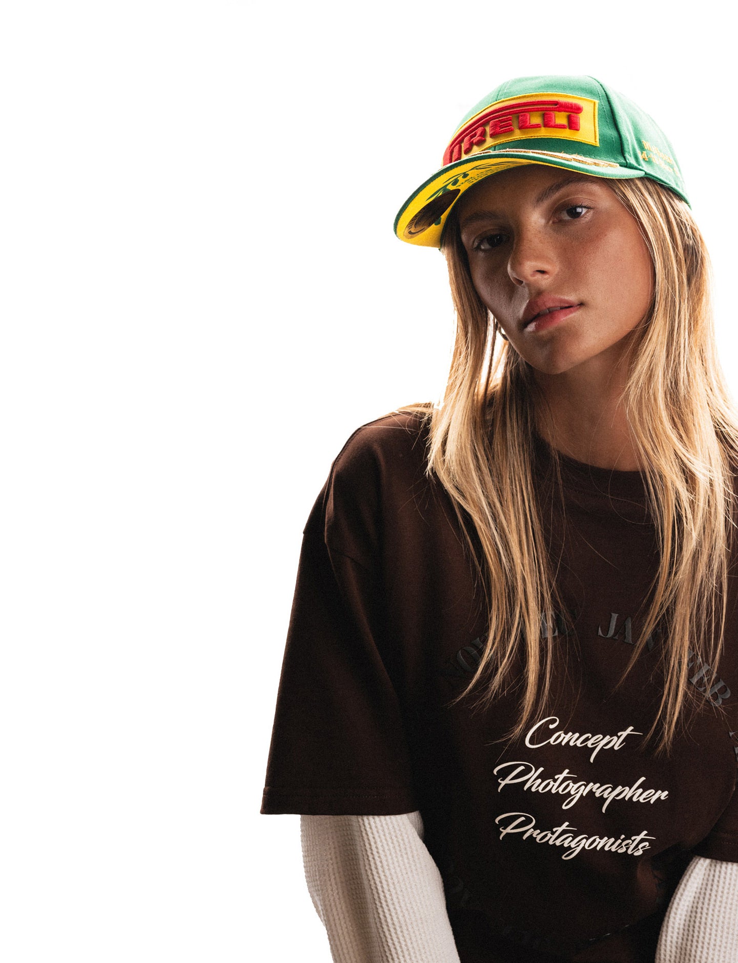 Person wearing a brown Pirelli t-shirt with text and a green and yellow Pirelli cap on a white background