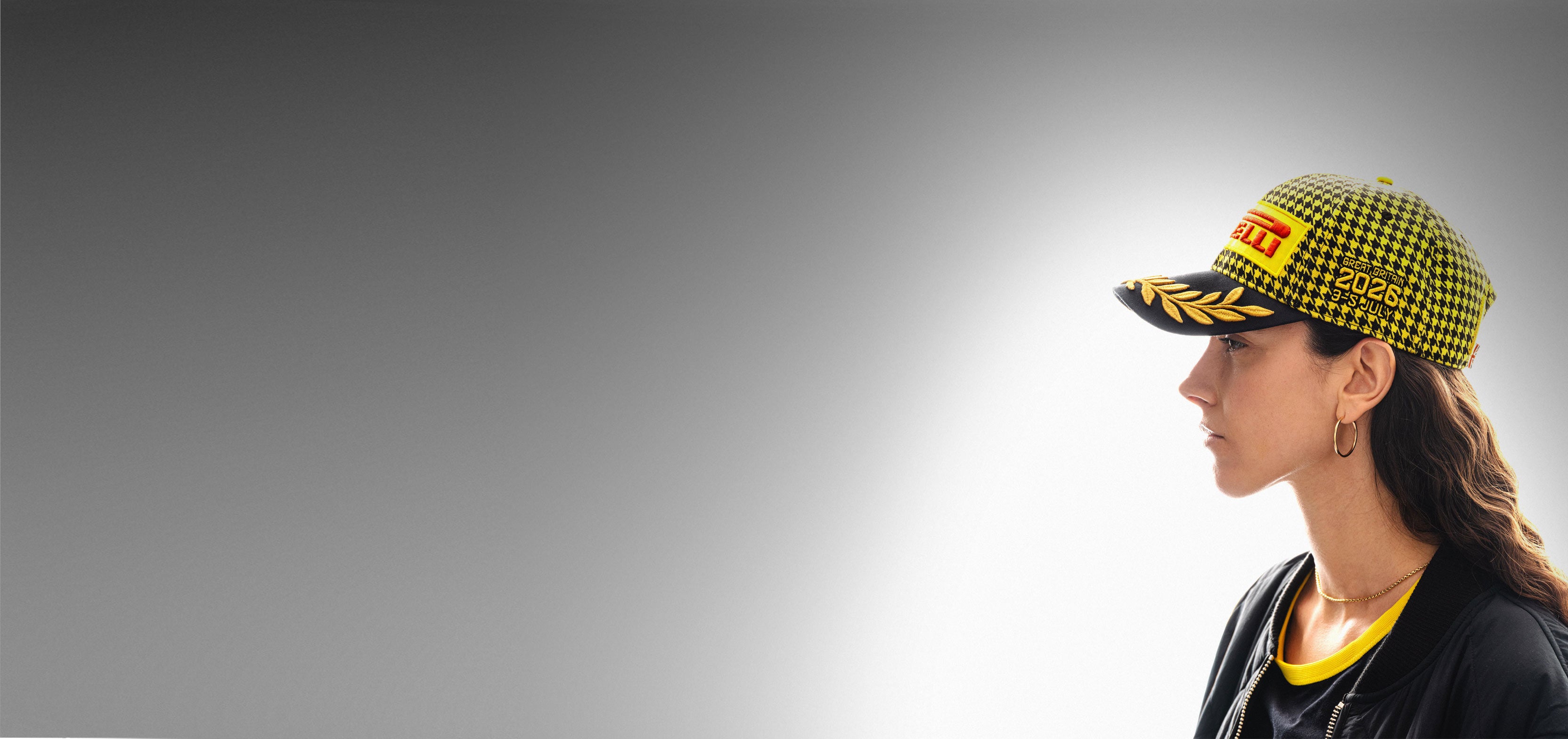 Person wearing a yellow and black checkered Pirelli Podium Cap 2026 Silverstone F1®