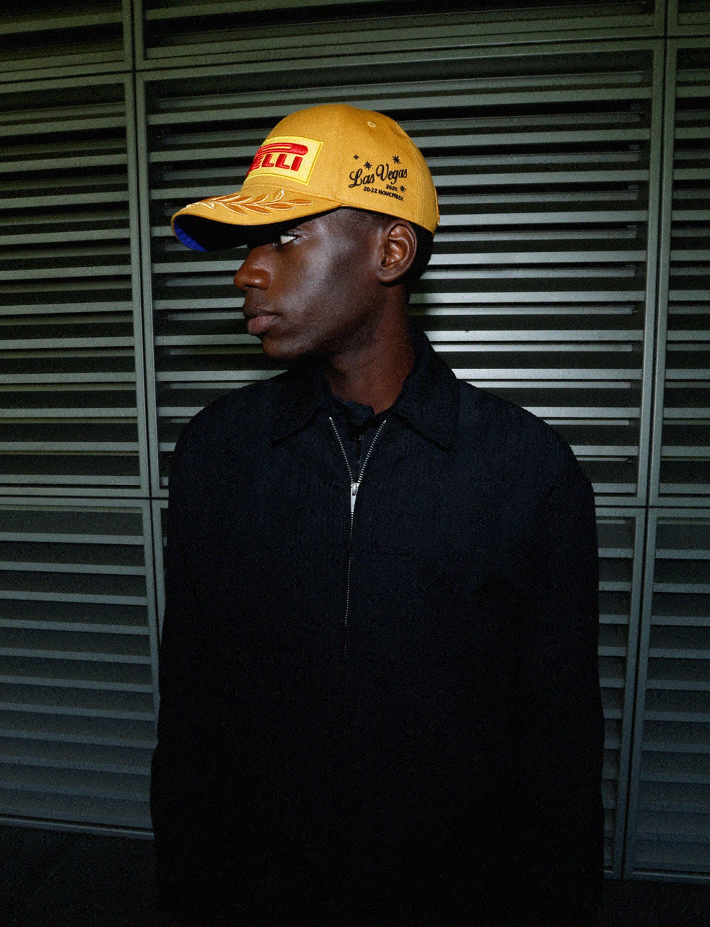 Person wearing a gold Pirelli Vegas cap against a metallic background