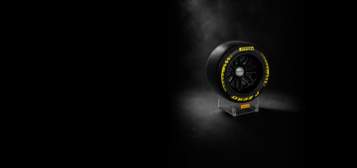 A Pirelli P Zero F1® race tire displayed upright on a clear acrylic stand against a dark, smoky studio background. The tire is black with bright yellow lettering and checkered accents, and the Pirelli logo is visible on both the tire sidewall and the center cap.